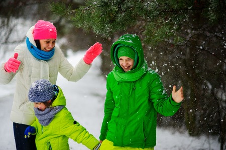 Mother with two sons on walk in winter day. The family stands under a big pine. It is snowing. All very much rejoice. Walks in the winter park are useful to health.の写真素材