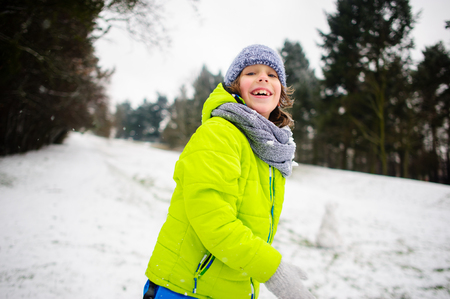 Boy of school age in bright winter overalls plays snowballs. Ground is slightly covered with the first snow. Child throws into someone a snowball. Children adore winter and snow.の写真素材