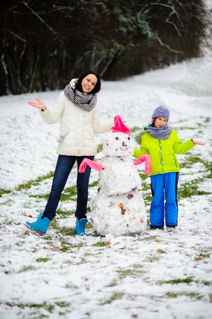 Mother with son have built snowman. Grass in park is slightly covered with snow. But charming young woman and her child are very glad to first snow. Snowman has turned out dirty, but very ridiculous.の写真素材