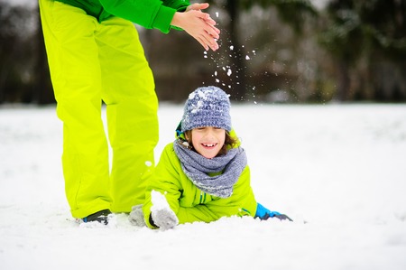 Two children joyfully play on snow. One boy in bright overalls lies, and the second pours on him snow. Children adore snow winter.の写真素材