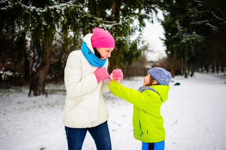 The young woman and her son cheerfully play in the winter park. The ground is covered with the first snow. Mother and the boy are dressed brightly and warmly. Winter walk pleases both.の写真素材