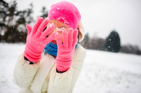 The charming young woman plays with someone in snowballs. She hides the face in hands. To the woman it is very cheerful. She is dressed in a bright ski suit.の写真素材
