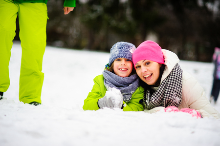 Charming young woman and her son cheerfully spend time in the winter park. They are dressed in bright warm ski suits. Both look out because of a big snowdrift also smile. On walk they are not one.の写真素材
