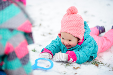 The little girl lies on snow and smiles. Snow gives the child joy. Someone was inclined over the baby. Children like winter games.の写真素材
