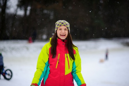 Winter portrait of the young woman in a bright ski suit and a knitted cap. It is snowing. Cute woman rejoices to winter and snow as the child.の写真素材