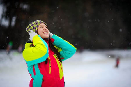 Winter portrait of the young woman in a bright ski suit and a knitted cap. It is snowing. Cute woman rejoices to winter and snow as the child.の写真素材