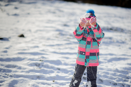 The girl of younger school age walks in the serene winter day. She throws a snowball. Her warm bright ski suit all in snow.の写真素材