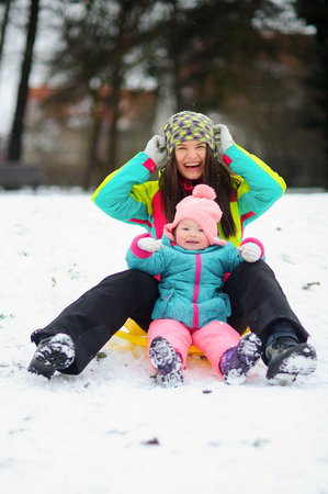 Young mother and her small the daughter were going to go down from a snow-covered hill on the sledge. Both warmly are also brightly dressed in ski suits.Mother and the daughter rejoice to winter.の写真素材