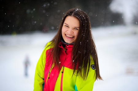 Lovely young woman brunette in a bright jacket on walk in winter day. It is snowing. The woman stands without headdress and joyfully laughs. Snowflakes lie on dark hair.の写真素材