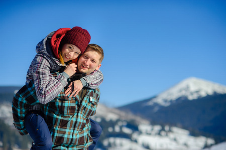 Young man holding his girlfriend on his shoulders. Girl embraces guy for neck. Against the backdrop of beautiful mountain scenery.の写真素材