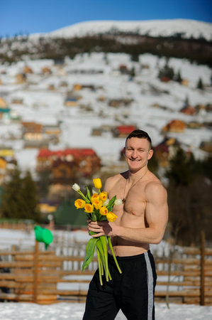 Young man with a bouquet of flowers against the background of snow-covered mountains. At man the brawny torso is naked. He friendly smiles.の写真素材
