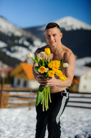Young man with a bouquet of flowers against the background of snow-covered mountains. At man the brawny torso is naked.の写真素材