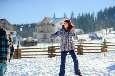 Guy and girl play snowballs. Serene winter day. Ground is covered with snow. In the distance coniferous forest. To young people it is very cheerful.の写真素材