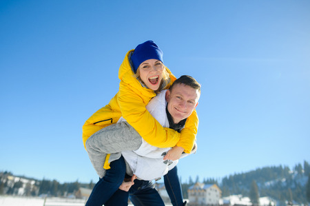 Young man holding his girlfriend on his shoulders. Girl embraces guy for neck. Young people look in the camera and cheerfully smile. Against the background of the blue sky.の写真素材