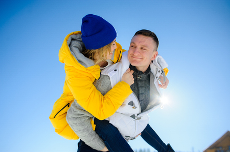 Young man holding his girlfriend on his shoulders. Girl embraces guy for neck. Young people look at each other with love and tenderness. Against the background of the blue sky.の写真素材