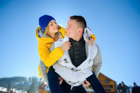 Young man holding his girlfriend on his shoulders. Girl embraces guy for neck. Young people look at each other with love and tenderness. Against the background of the blue sky.の写真素材