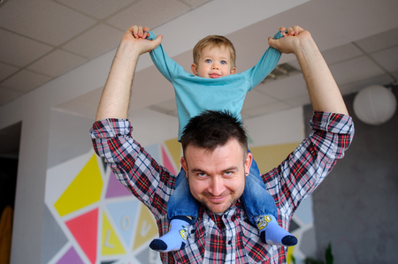 Little boy sits on the shoulders of his father. Young man playing with a child. Both the daddy and the kid smile.の写真素材
