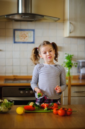 Girl 8-9 years old in the kitchen slicing vegetables for a salad. On the table there are a lot of different vegetables. They look very appetizing. The habit of healthy food from childhood.の写真素材
