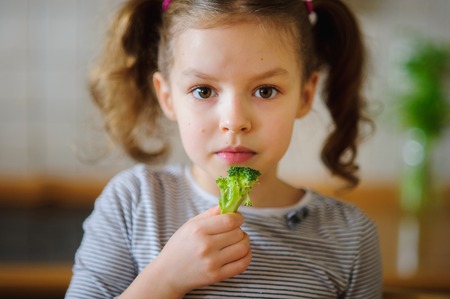 Cute fair-haired girl eats fresh broccoli. She does it with pleasure. Healthy food since the childhood.の写真素材