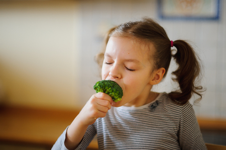 Cute fair-haired girl eats fresh broccoli. She does it with pleasure. Healthy food since the childhood.の写真素材
