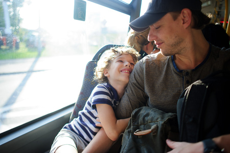 The young man goes by the bus together with the son. The father and the son sit next with each other and communicate with pleasure. On their faces expression of love and joy.の写真素材