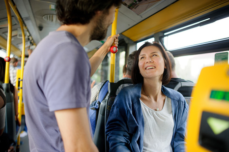Young couple in inside of the city bus. The girl sits, the fellow stands nearby. Young people look at each other and smile.の写真素材
