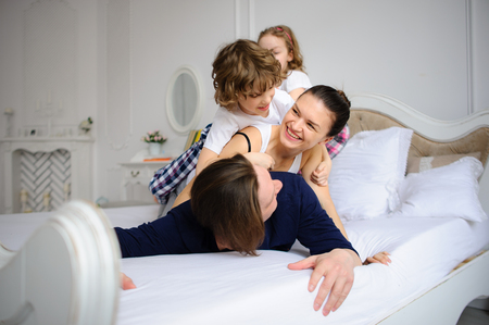 Morning of the day off in a happy family. Cheerful beginning of day. Mother the father and two children have started comic battle on a bed.の写真素材