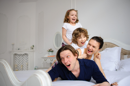 Morning of the day off in a happy family. Cheerful beginning of day. Mother the father and two children have started comic battle on a bed.の写真素材