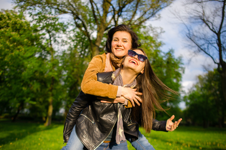 Two cute young women cheerfully spend time in the spring park. Women have a playful mood. Warm sunny day. Girlfriends enjoy the nature and communication.の写真素材