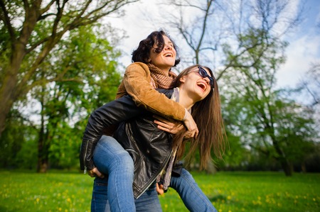Two cute young women cheerfully spend time in the spring park. Women have a playful mood. Warm sunny day. Girlfriends enjoy the nature and communication.の写真素材