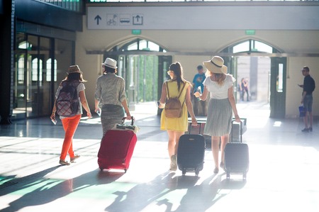 Group of young tourists at the station. In hands at girls suitcases, tickets, passports. Summer tourism. View from a back.の写真素材