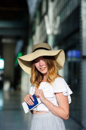 Pretty girl in a wide-brimmed hat with the passport and tickets in a hand. Girl posing. Railway station. Summer holiday.の写真素材