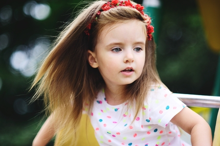 Portrait of the charming girl of 4-5 years. Beautiful long fair hair. A wreath from red colors on the head. Expressive gray-blue eyes. Bright lips.の写真素材