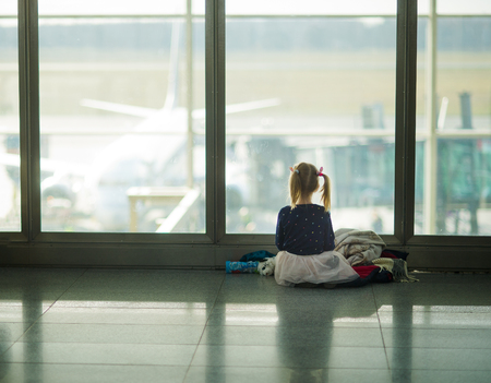The little girl sits near a big window at the airport. The child looks at big planes on a runway.の写真素材