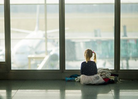 The little girl sits near a big window at the airport. The child looks at big planes on a runway.の写真素材