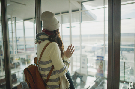 A woman with a backpack standing at the large window in the airport. She is watching the airplanes on the airfield.の写真素材