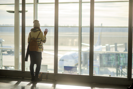 A woman with a backpack standing at the large window in the airport. She is watching the airplanes on the airfield.の写真素材