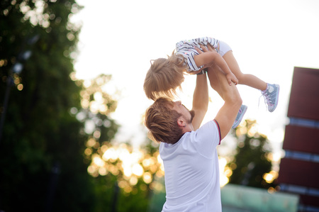 Young dad is playing with a charming little daughter. Man throws up a child. The girl laughs happily.の写真素材