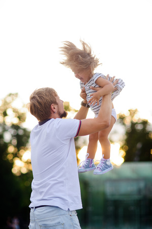 Young dad is playing with a charming little daughter. Man throws up a child. The girl laughs happily.の写真素材