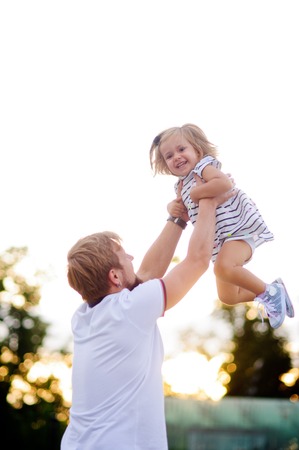 Young dad is playing with a charming little daughter. Man throws up a child. The girl laughs happily.の写真素材
