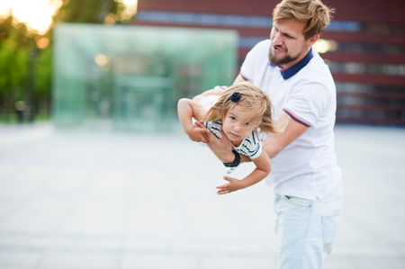 Young dad is playing with a charming little daughter. The man holds the baby on handsand is turned together with her. The child laughs with pleasure.の写真素材