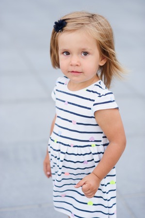 Portrait of a two year old girl in a striped dress. Nice face, short blond hair, serious look.の写真素材