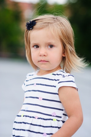 Portrait of a two year old girl in a striped dress. Nice face, short blond hair, serious look.の写真素材