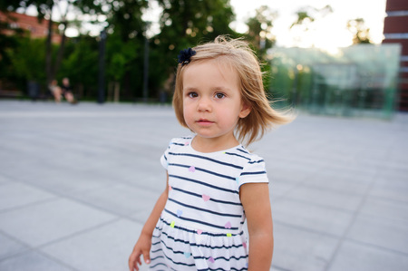 Portrait of a two year old girl in a striped dress. Nice face, short blond hair, serious look.の写真素材