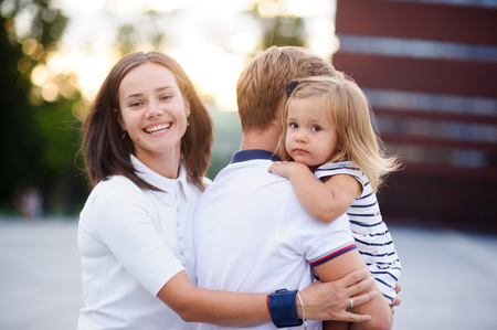 Portrait of a young united family. Father keeps a small daughter in his arms. Woman gently embraces husband and daughter.の写真素材