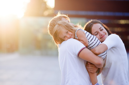 Portrait of a young united family. Father keeps a small daughter in his arms. Woman gently embraces husband and daughter.の写真素材
