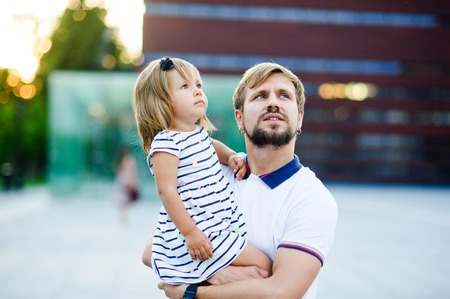 Young father holds the little daughter on hands. Man gently presses to himself the child.の写真素材