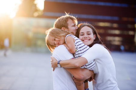 Portrait of a young united family. Father keeps a small daughter in his arms. Woman gently embraces husband and daughter.の写真素材