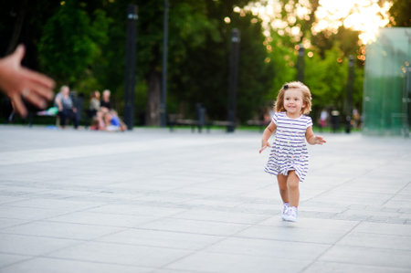 Adorable little girl runs towards the parent hands. Warm summer day. Baby is very fun.の写真素材