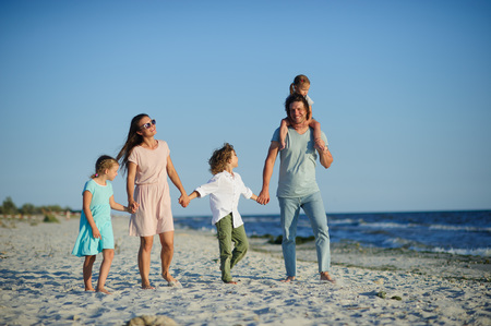Big happy family walking at the beach. Mom, dad and three children. The blue sky, the sun, fresh sea wind. Pleasure from nature and communication.の写真素材